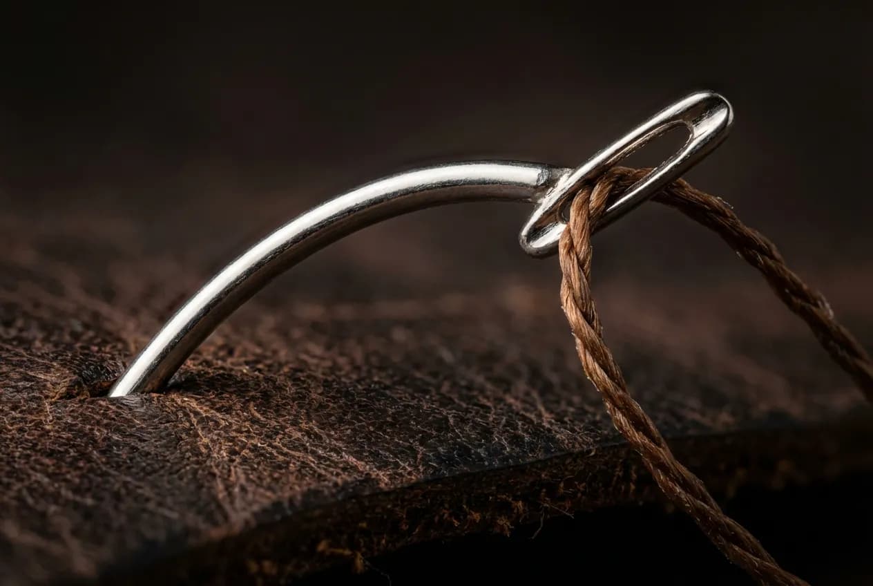 Gros plan macro aiguille courbe de tapissier traversant du cuir épais