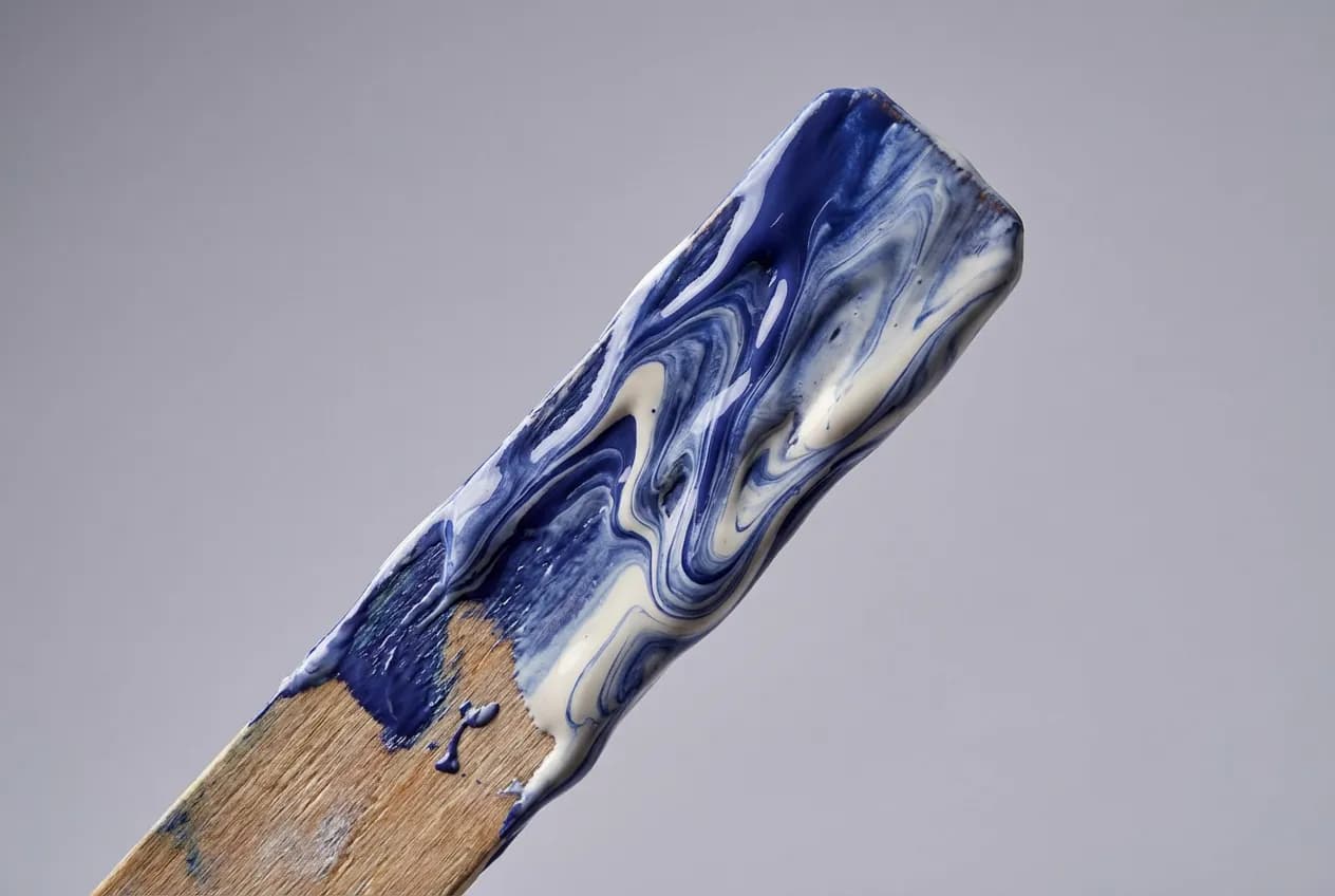 Peut-on mélanger 2 peintures différentes ? Guide complet Gros plan sur un bâtonnet de mélange enduit de peinture bleue et blanche