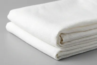 Pile de nappes blanches en lin fraîchement lavées et pliées, gros plan sur la texture.
