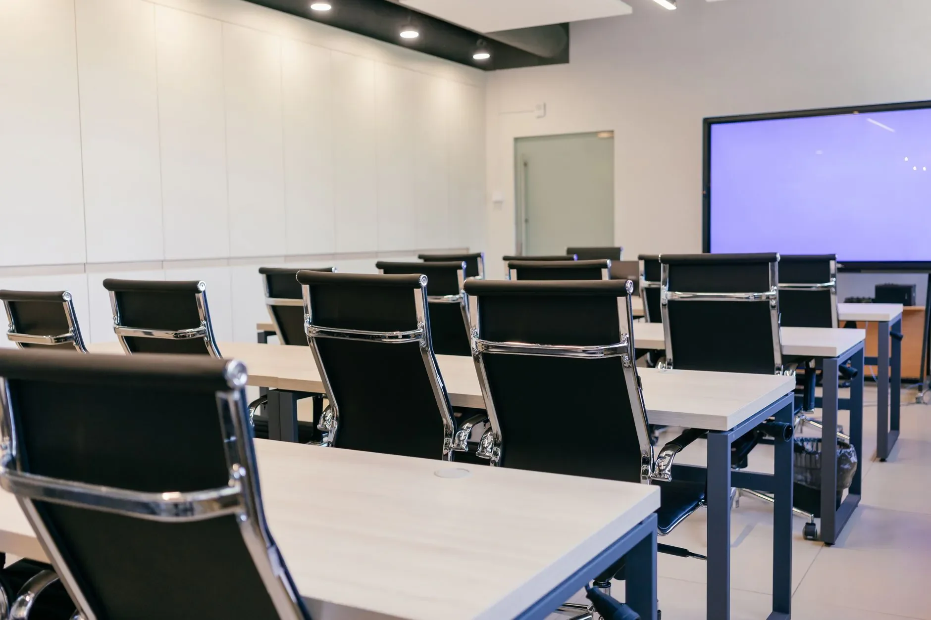 Salle de conférence spacieuse et moderne avec des chaises noires et un écran de projection.