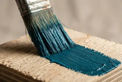 Gros plan pinceau appliquant peinture bleue sur surface contreplaqué.