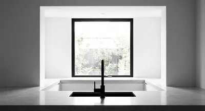 Plan centré minimaliste d'un évier noir sous une fenêtre de cuisine lumineuse