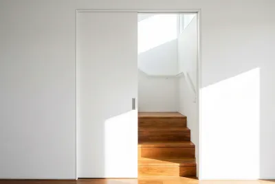 Vue minimaliste d'une porte coulissante blanche entrouverte sur des marches d'escalier en bois