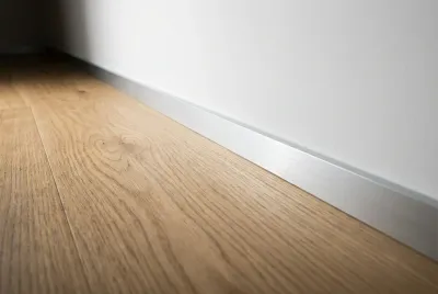 Gros plan sur une finition de plinthe affleurante moderne entre parquet et mur blanc