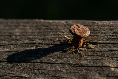 Gros plan iconique sur un clou ressortant d'une lame de parquet en bois, une cause possible de grincement.