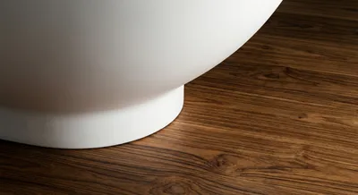 Détail minimaliste du contact entre une baignoire blanche et un sol en teck texturé.