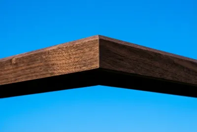 Gros plan sur la ligne graphique et épurée d'un débord de toit en bois foncé, créant un contraste saisissant avec le ciel.