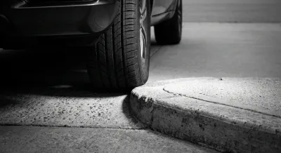 Miniature d'une roue de voiture touchant une rampe d'accès en béton, avec un contraste élevé.
